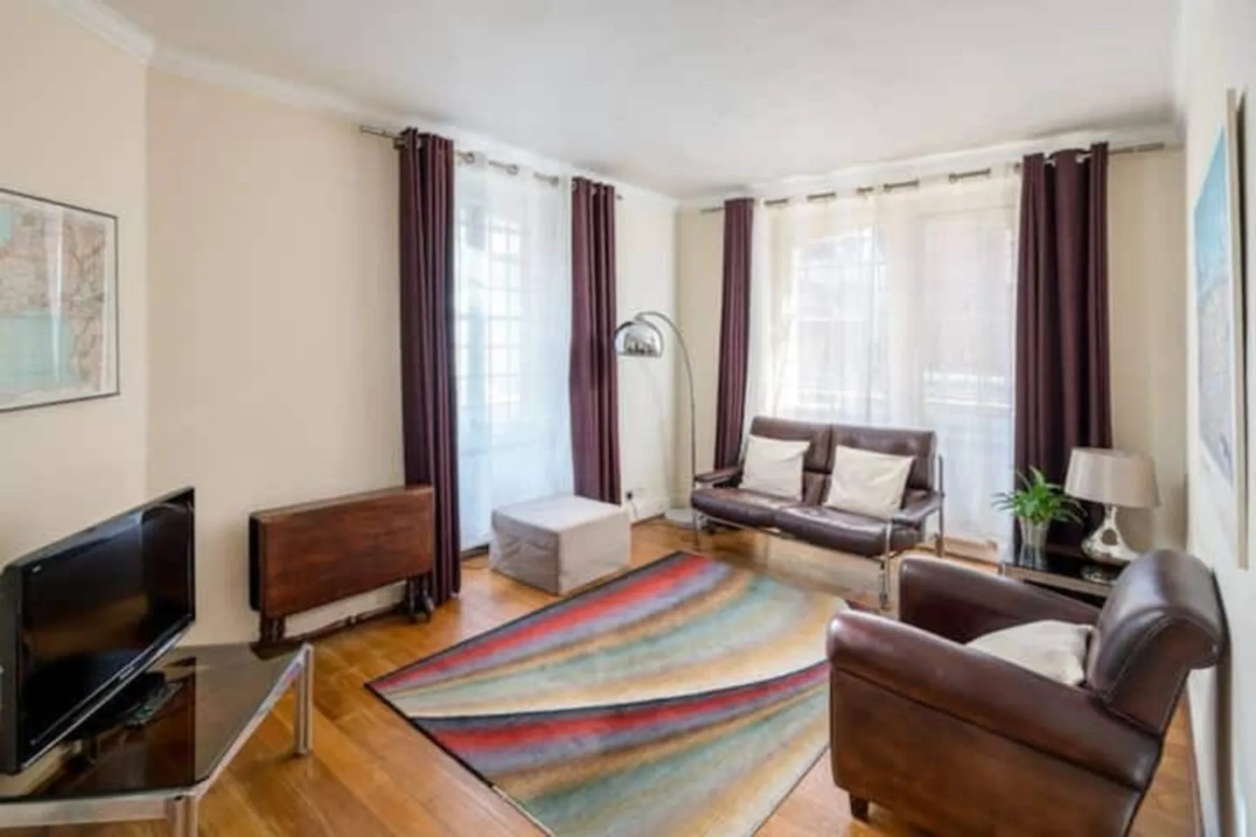 A living room with seating around a colorful striped rug and large windows.