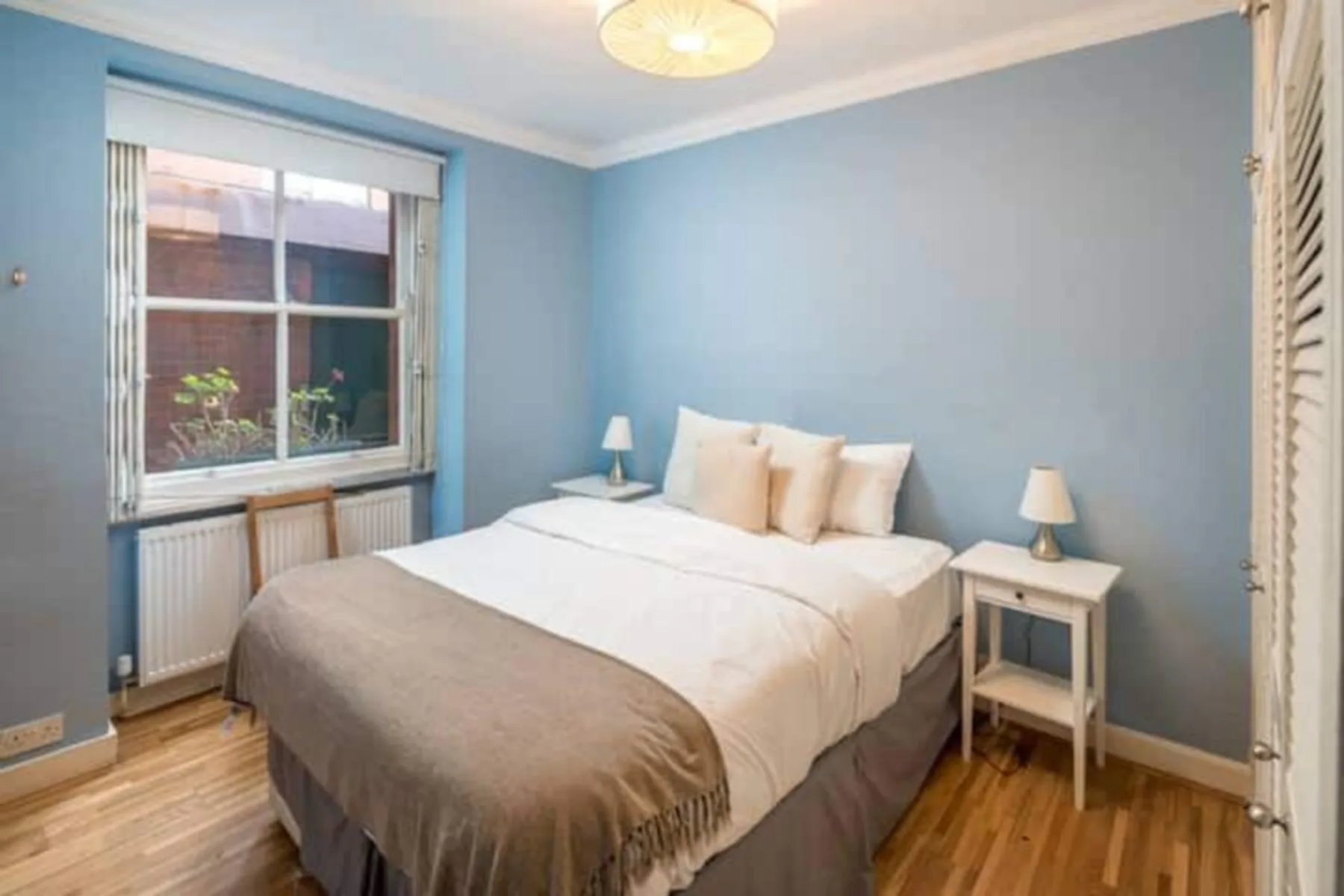 Un dormitorio con una cama arreglada, mesillas de noche y una ventana amplia.