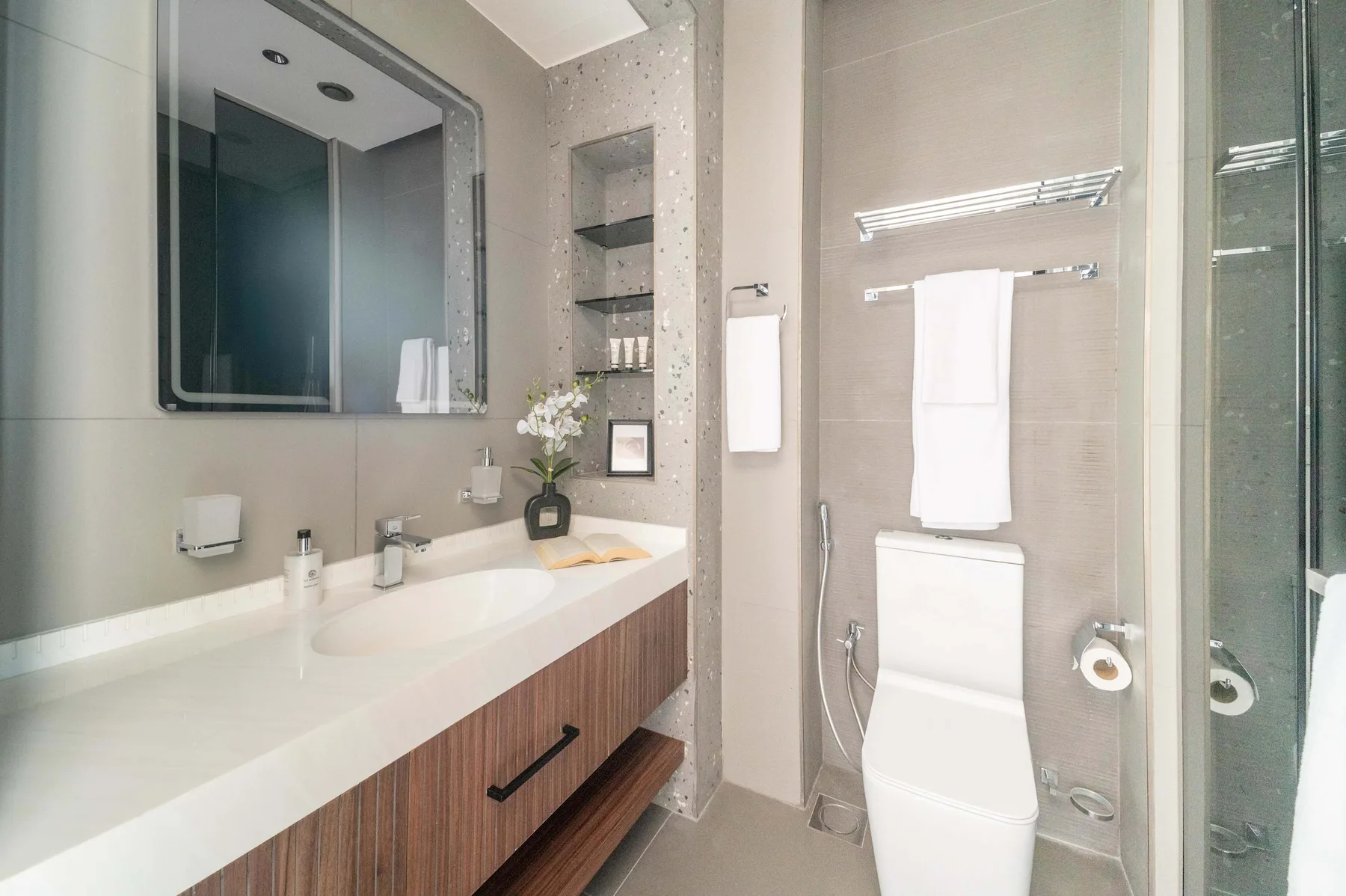 Un baño moderno con una encimera larga con lavabo, inodoro y ducha de vidrio.