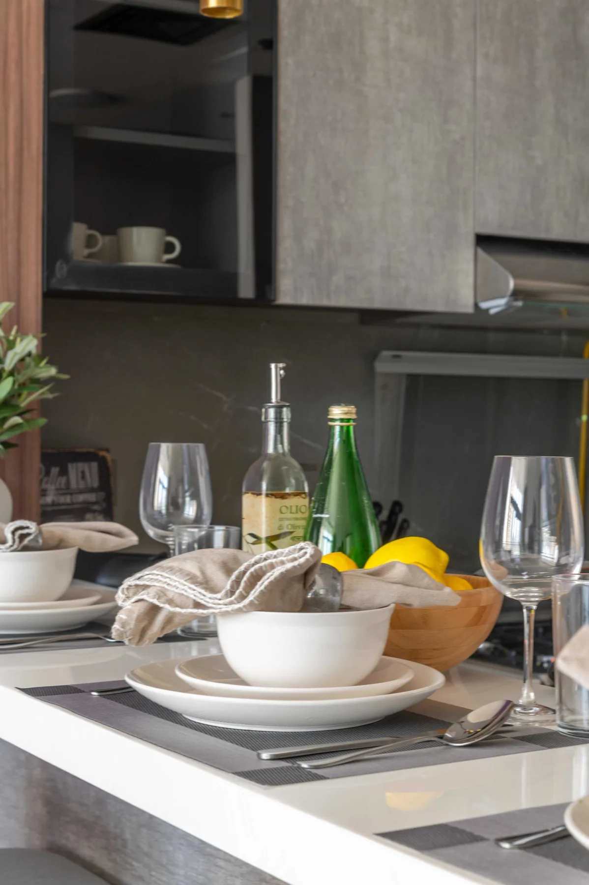 Una encimera de cocina moderna está preparada con platos, copas, botellas y un cuenco de limones.
