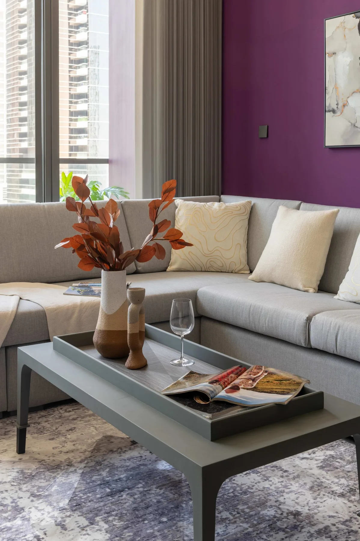 Una sala de estar con un sofá seccional claro y una mesa de centro junto a grandes ventanas.