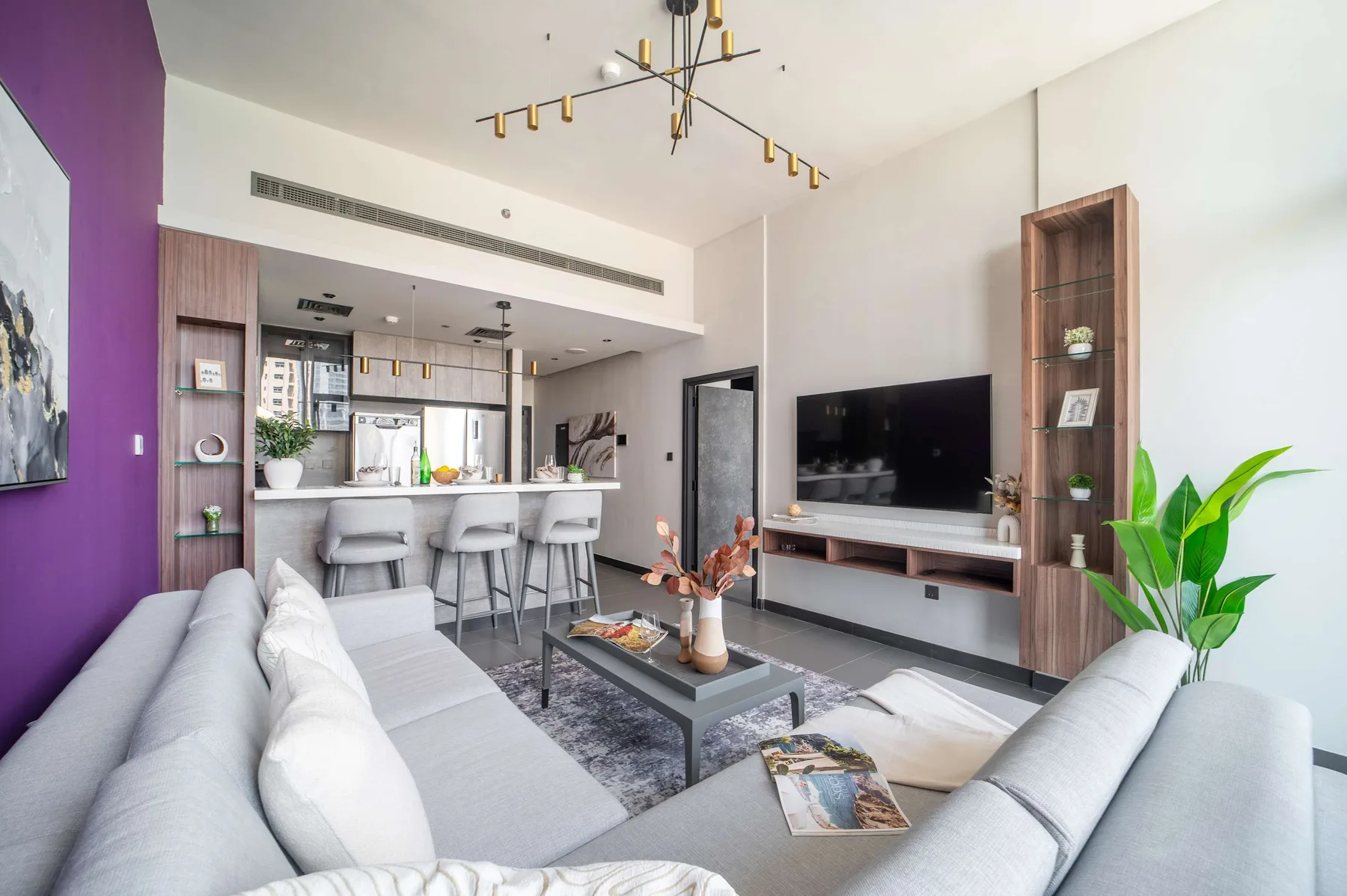 Una sala de estar moderna con asientos, televisión y una cocina abierta.
