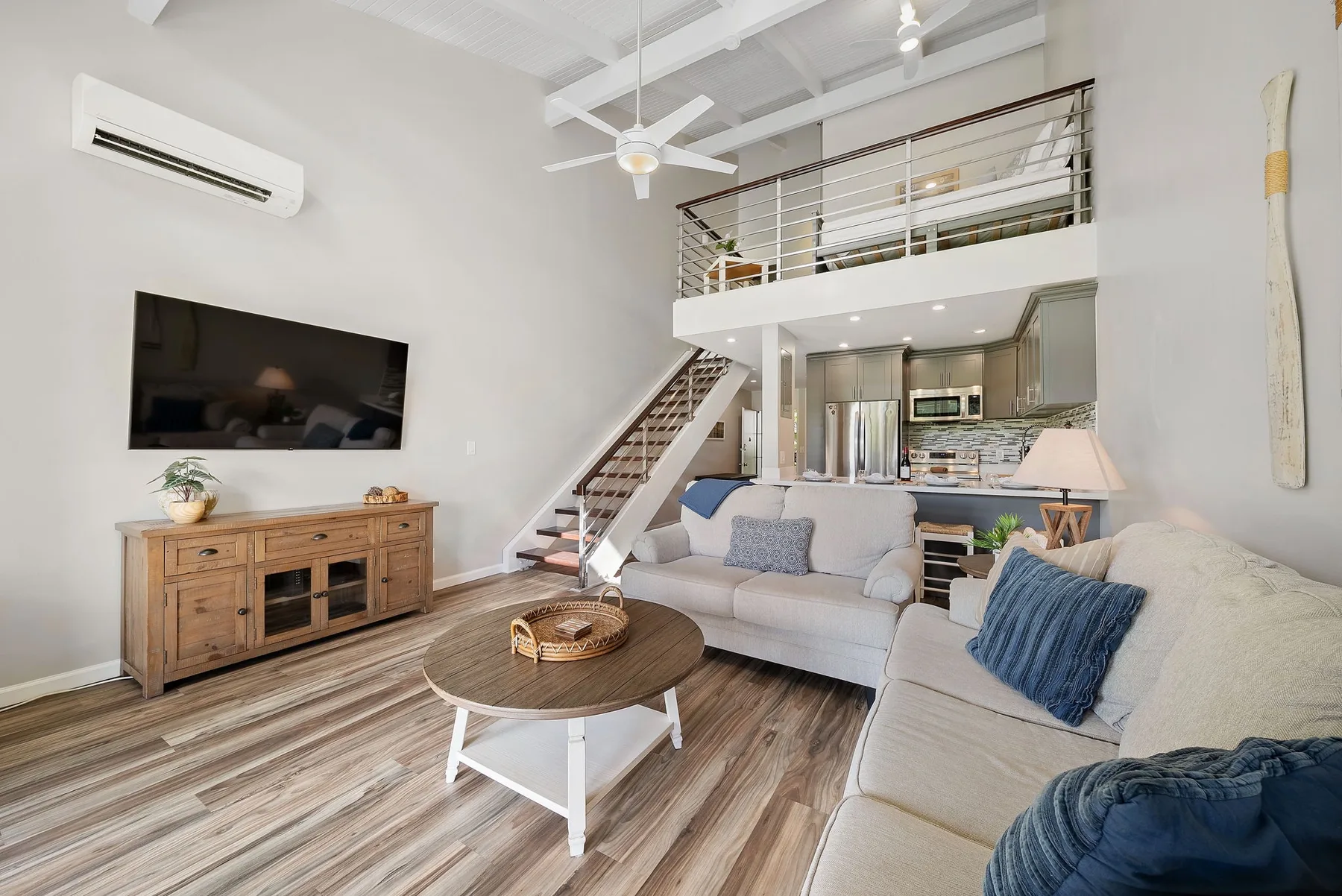 A bright living room with a sectional sofa, coffee table, and staircase to an upper level.
