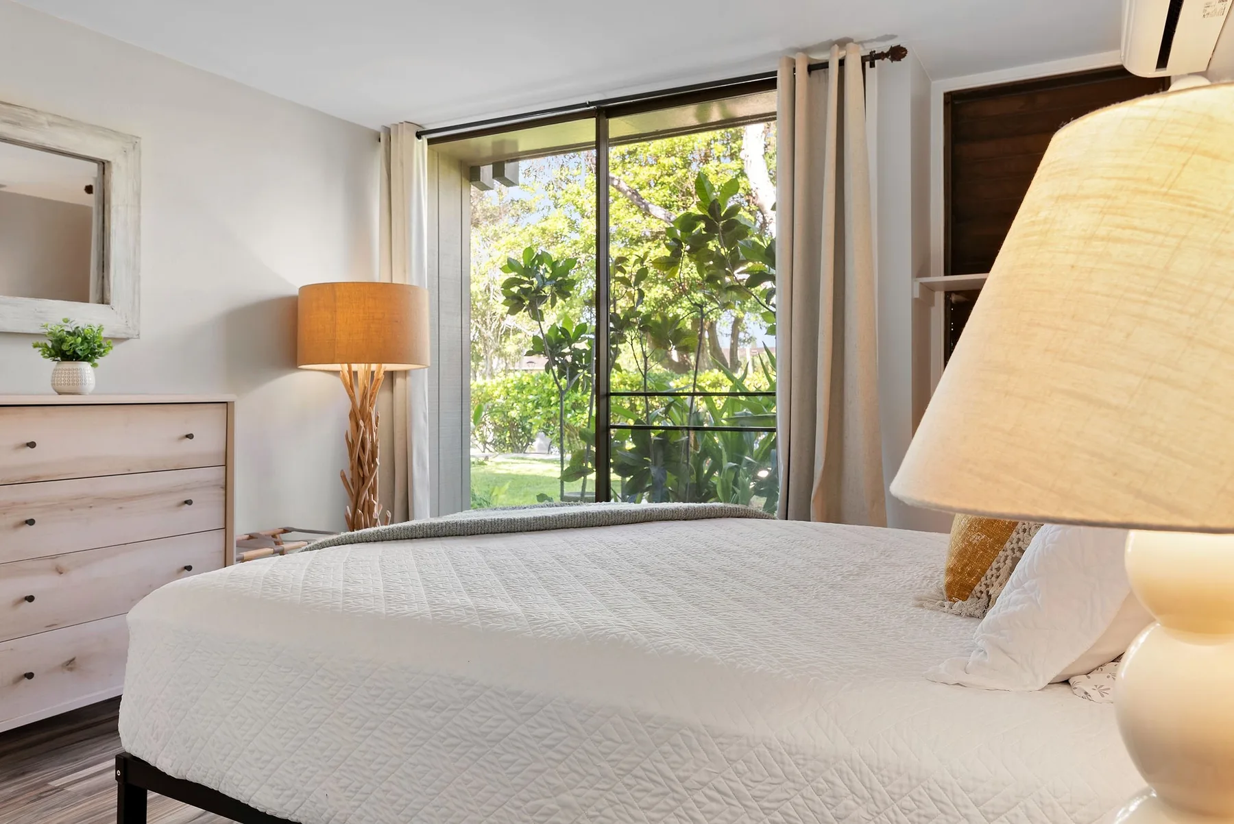 A bedroom with a bed beside a large window overlooking greenery.