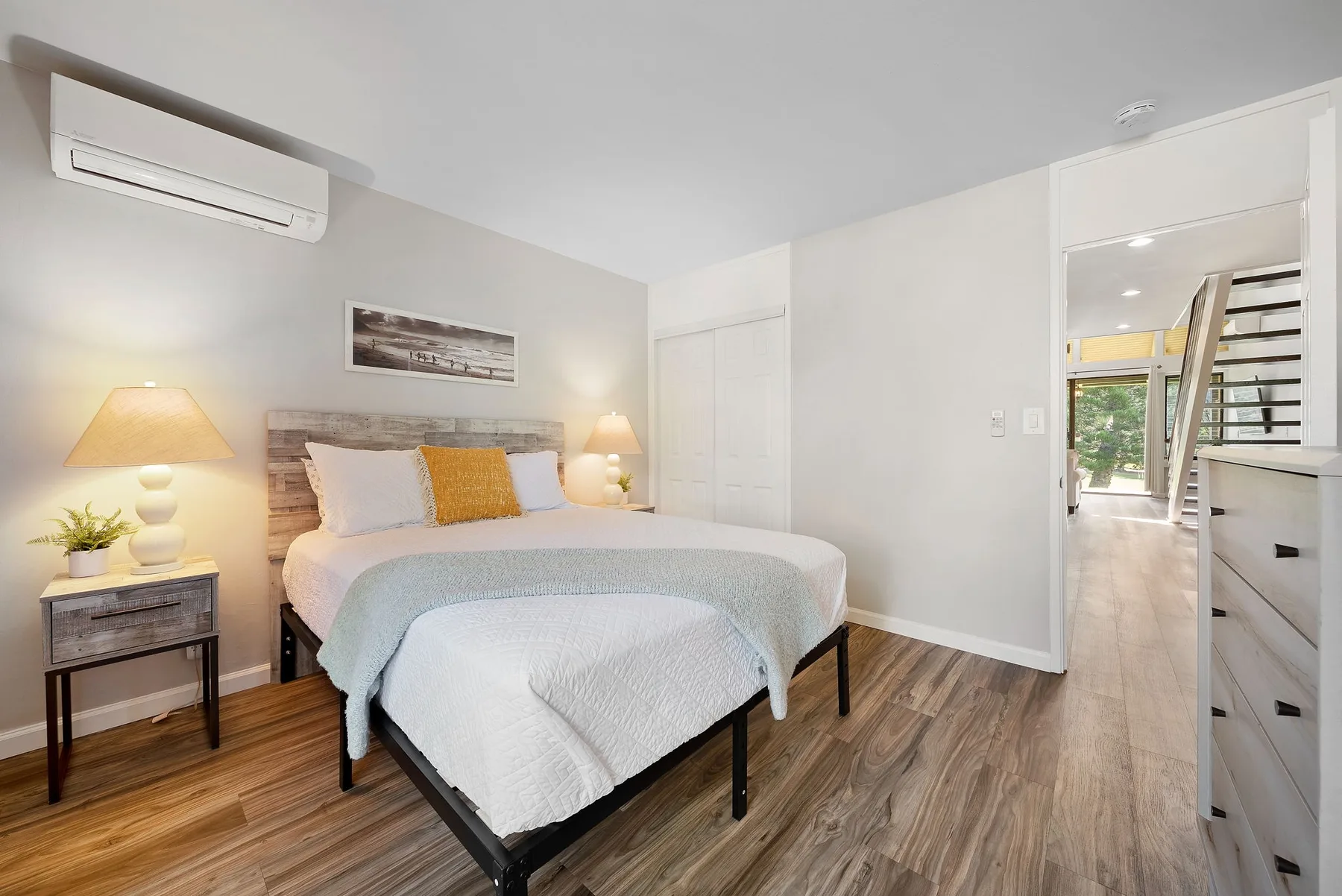 A bedroom with a bed, bedside tables, and a wall-mounted air conditioner.