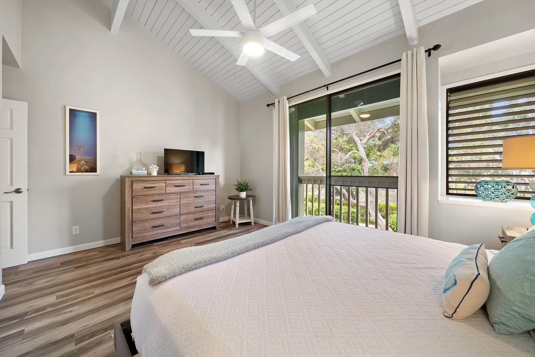 A bright bedroom with a bed, dresser, and sliding glass doors opening to a balcony.