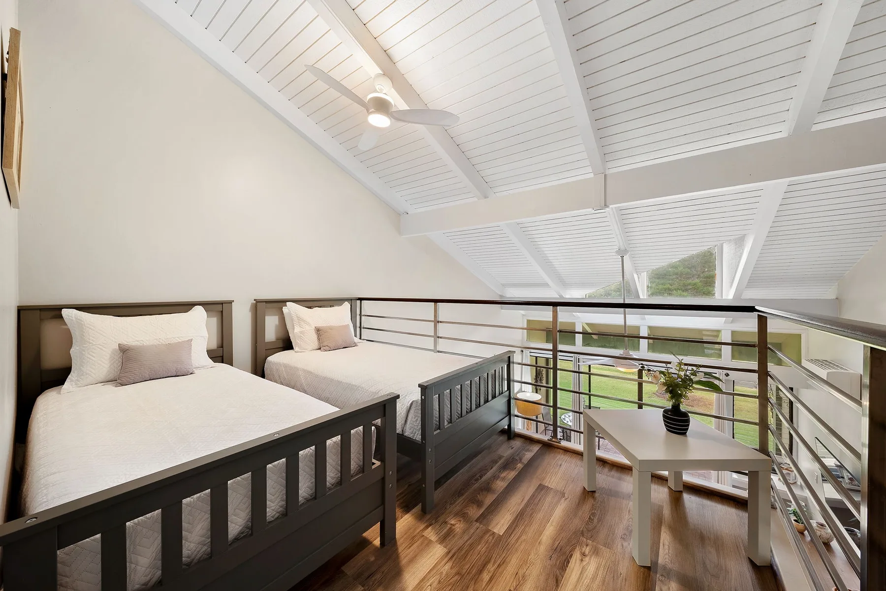 A loft bedroom with two beds and a small seating area beside the railing.
