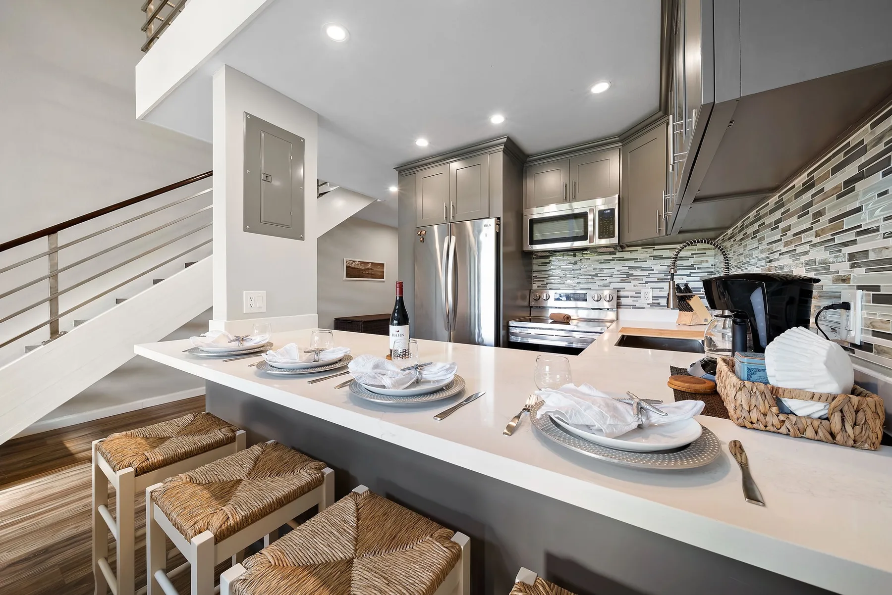 An open kitchen with a breakfast counter, stainless steel appliances, and woven stools.