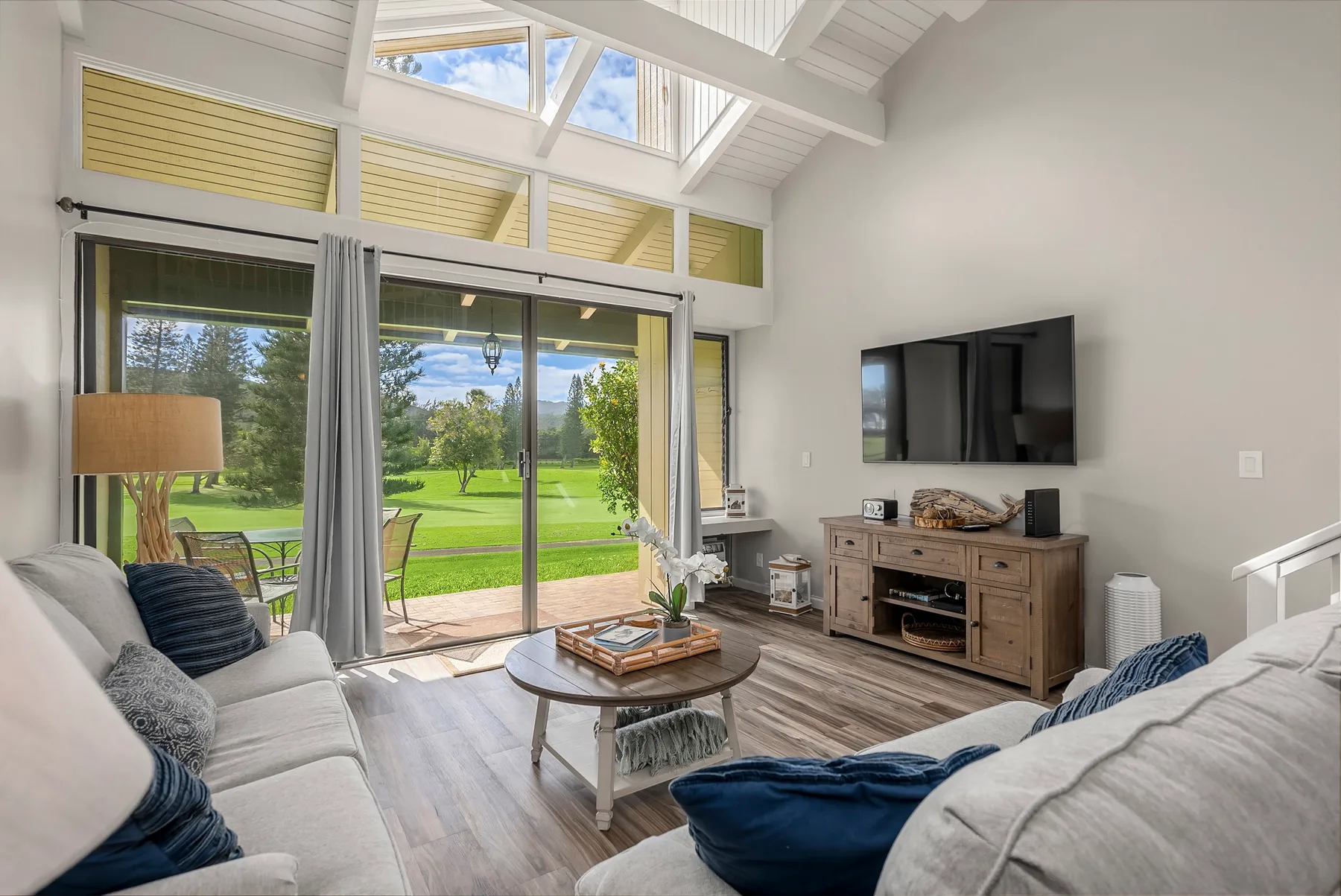 A bright living room with seating, a television, and glass doors opening onto a green lawn.