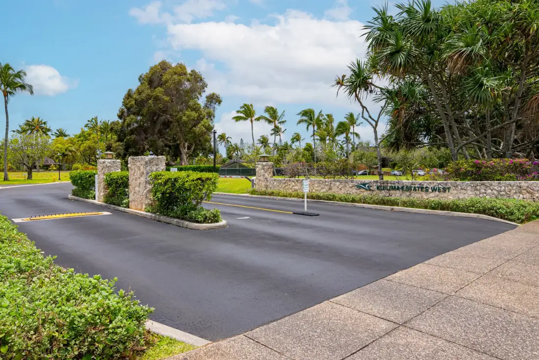 A landscaped entrance driveway runs past stone pillars and tropical greenery.
