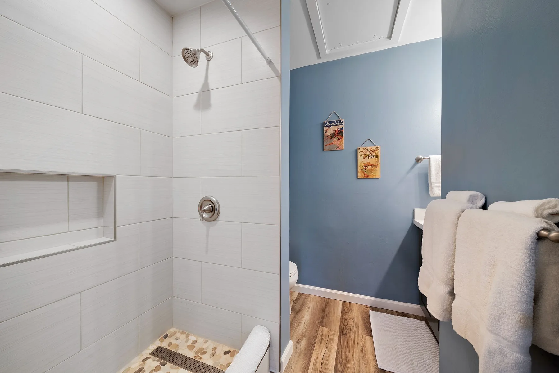 A tiled bathroom shower beside a blue wall and towel rack.