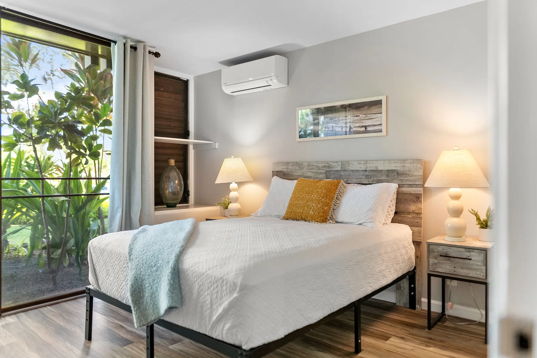A bright bedroom with a neatly made bed and a large window overlooking greenery.
