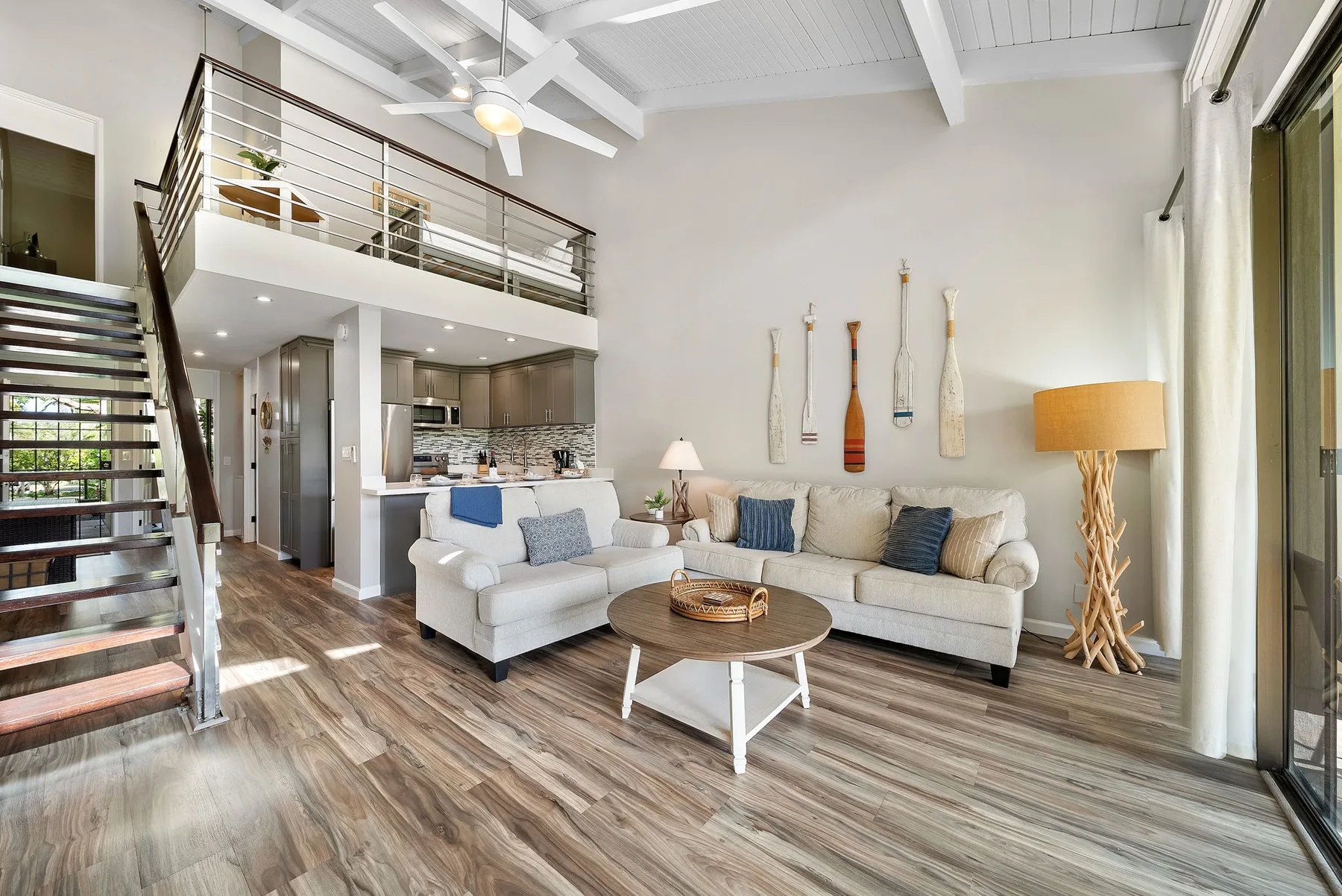 A bright living room with seating, a round coffee table, and a staircase.