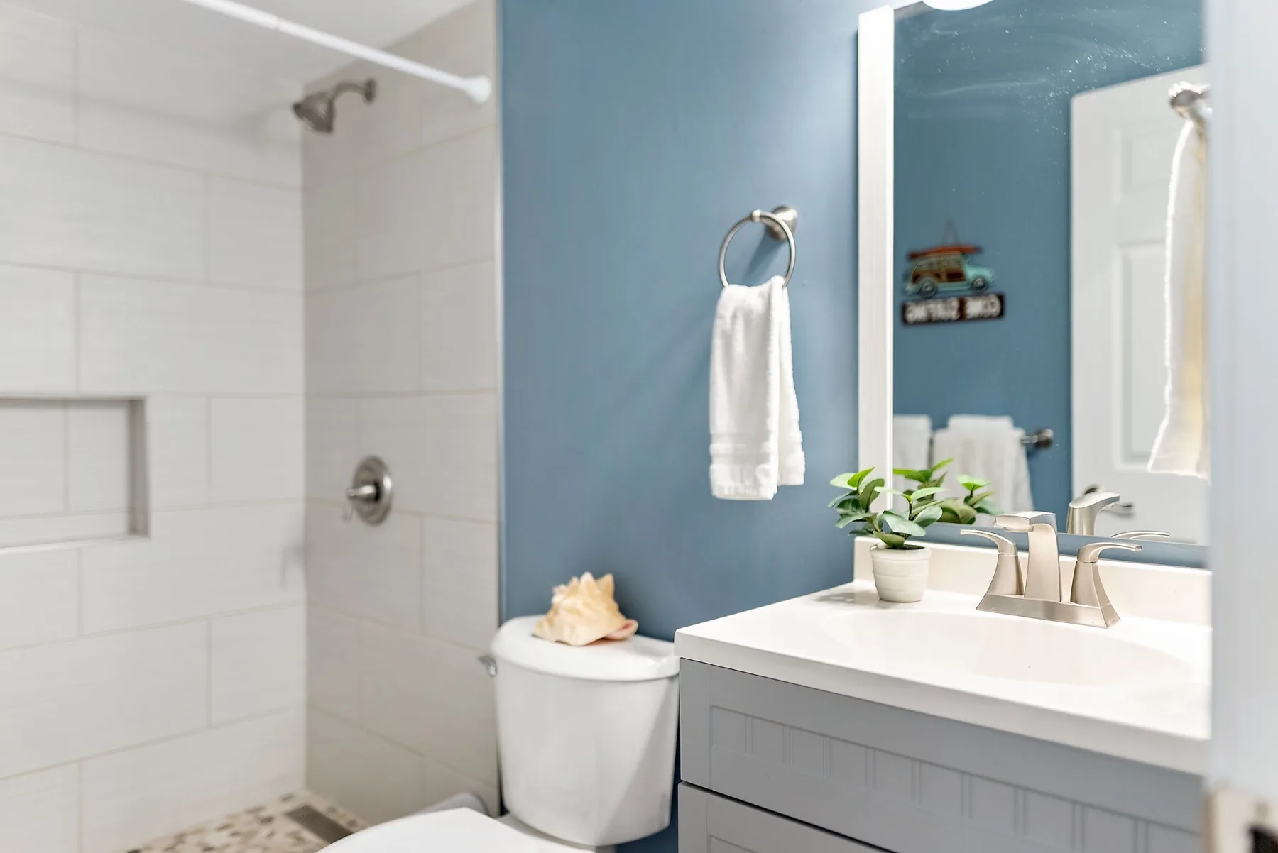 A bathroom with a shower, toilet, and sink beside a blue wall.