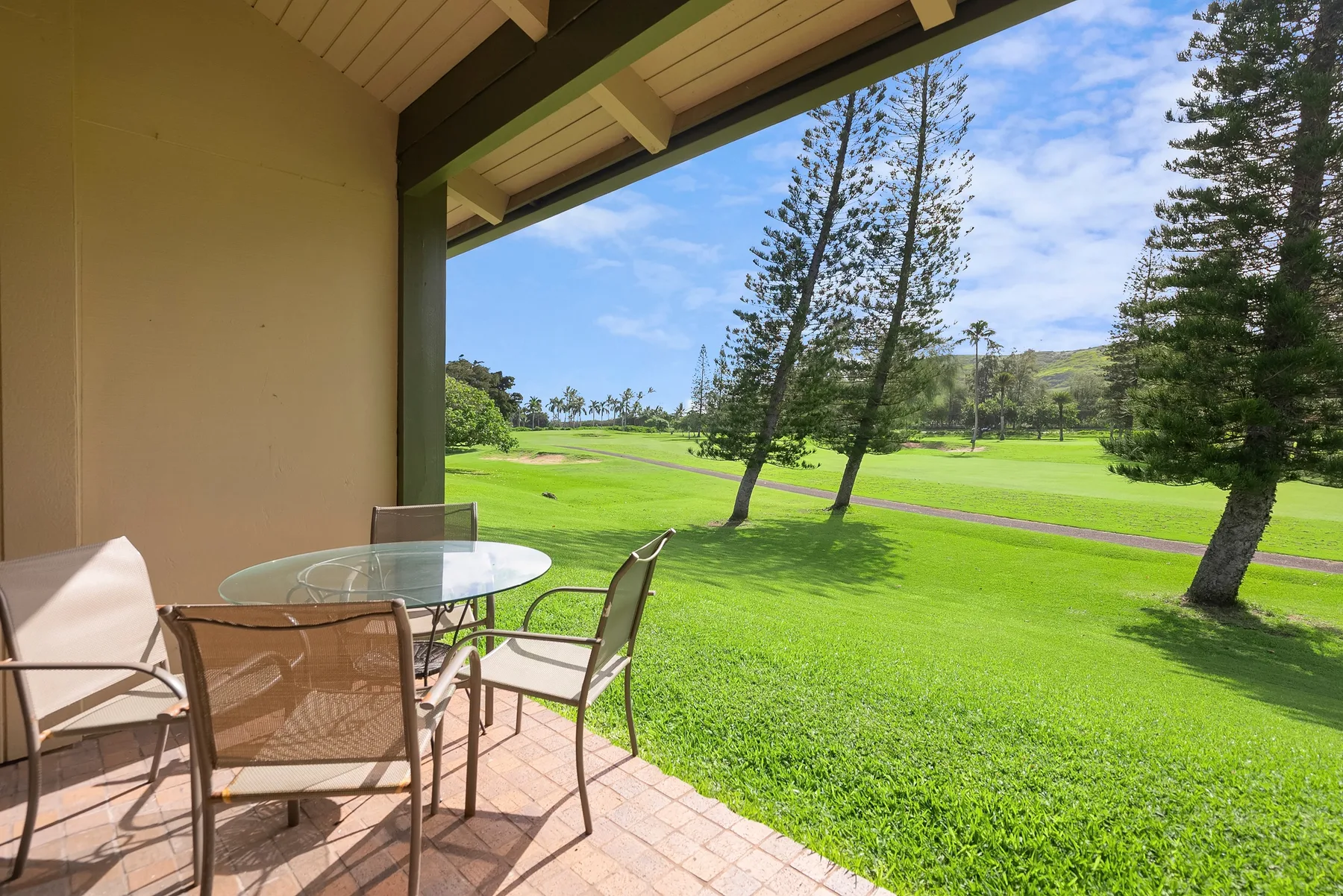 A covered patio with outdoor seating overlooks a broad green lawn and trees.