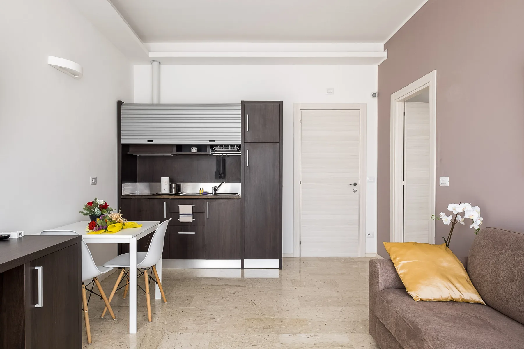Una cocina compacta y zona de estar con armarios oscuros y un sofá marrón.
