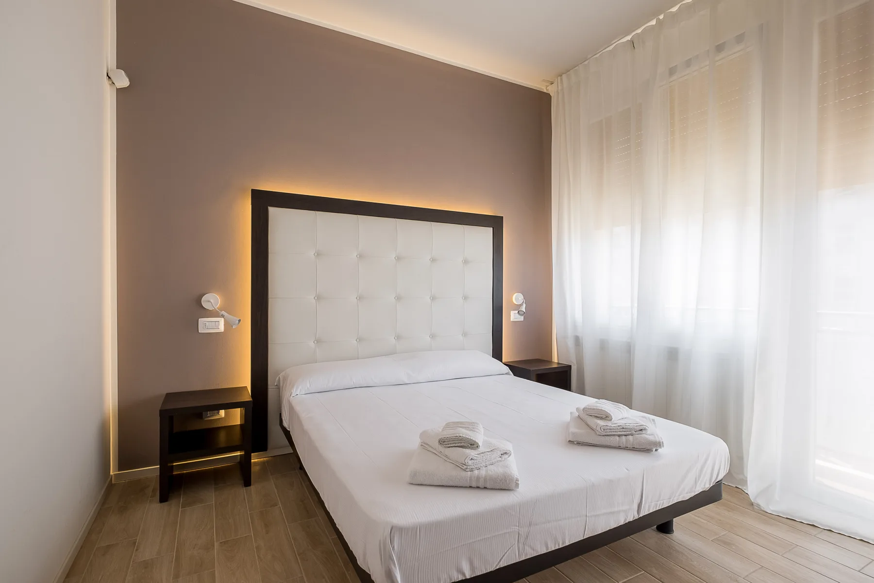 Un dormitorio con una cama bien tendida y cortinas translúcidas.