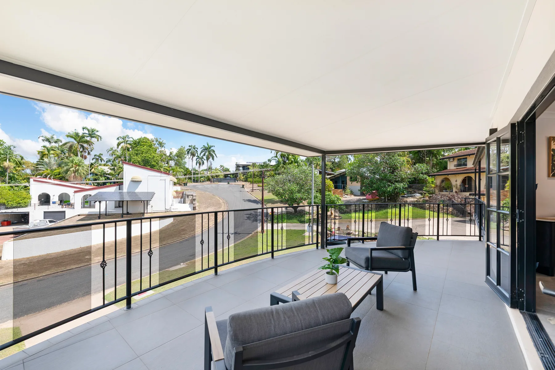 A covered balcony with outdoor seating overlooks nearby homes and greenery.