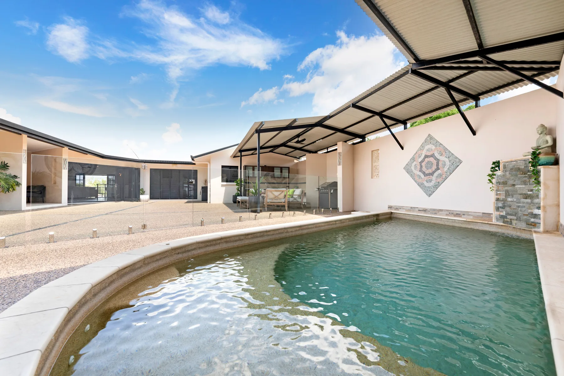 An outdoor swimming pool sits beside a covered patio with seating.