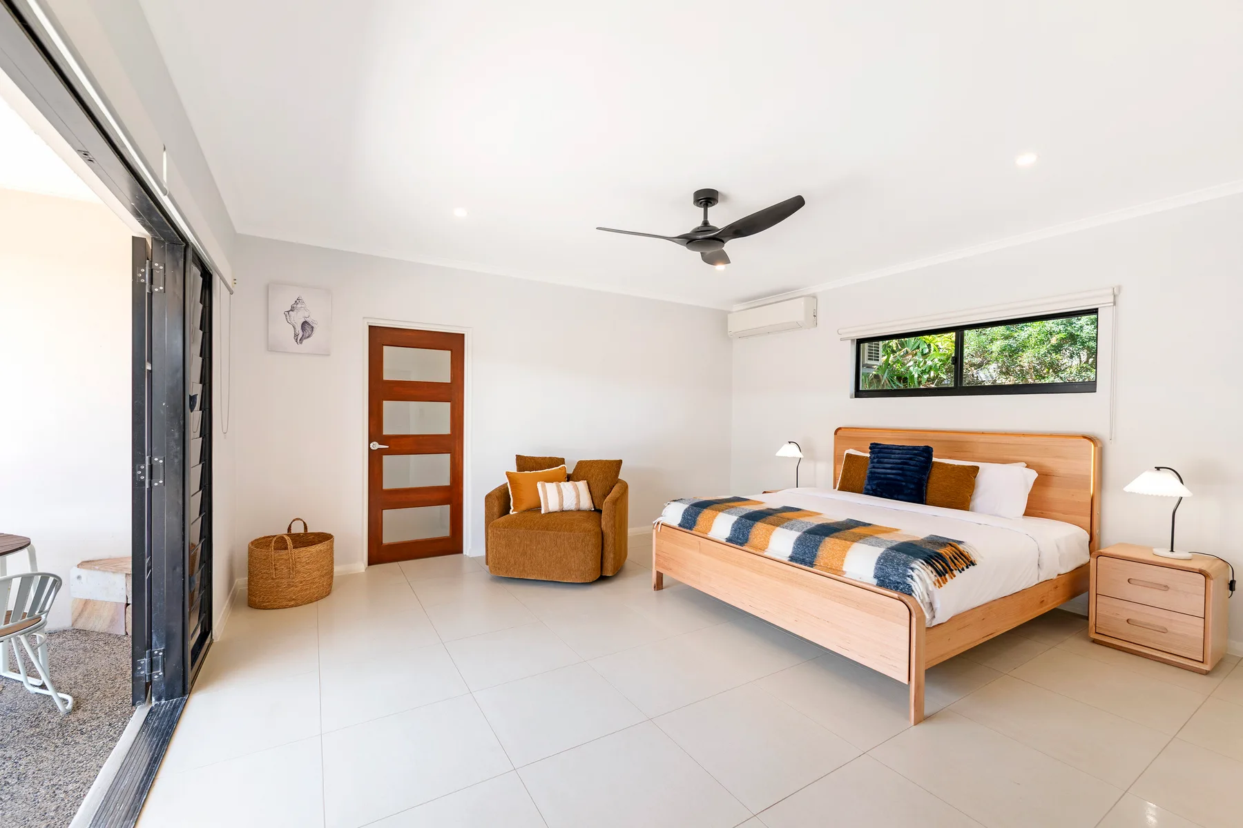 A bright bedroom with a bed, an armchair, and sliding glass doors opening onto a patio.