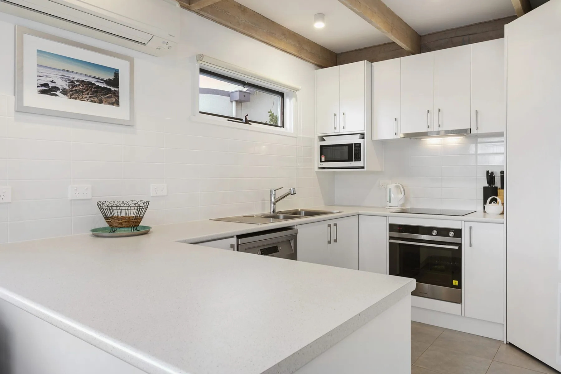 A bright kitchen with white cabinets, counters, and built-in appliances.