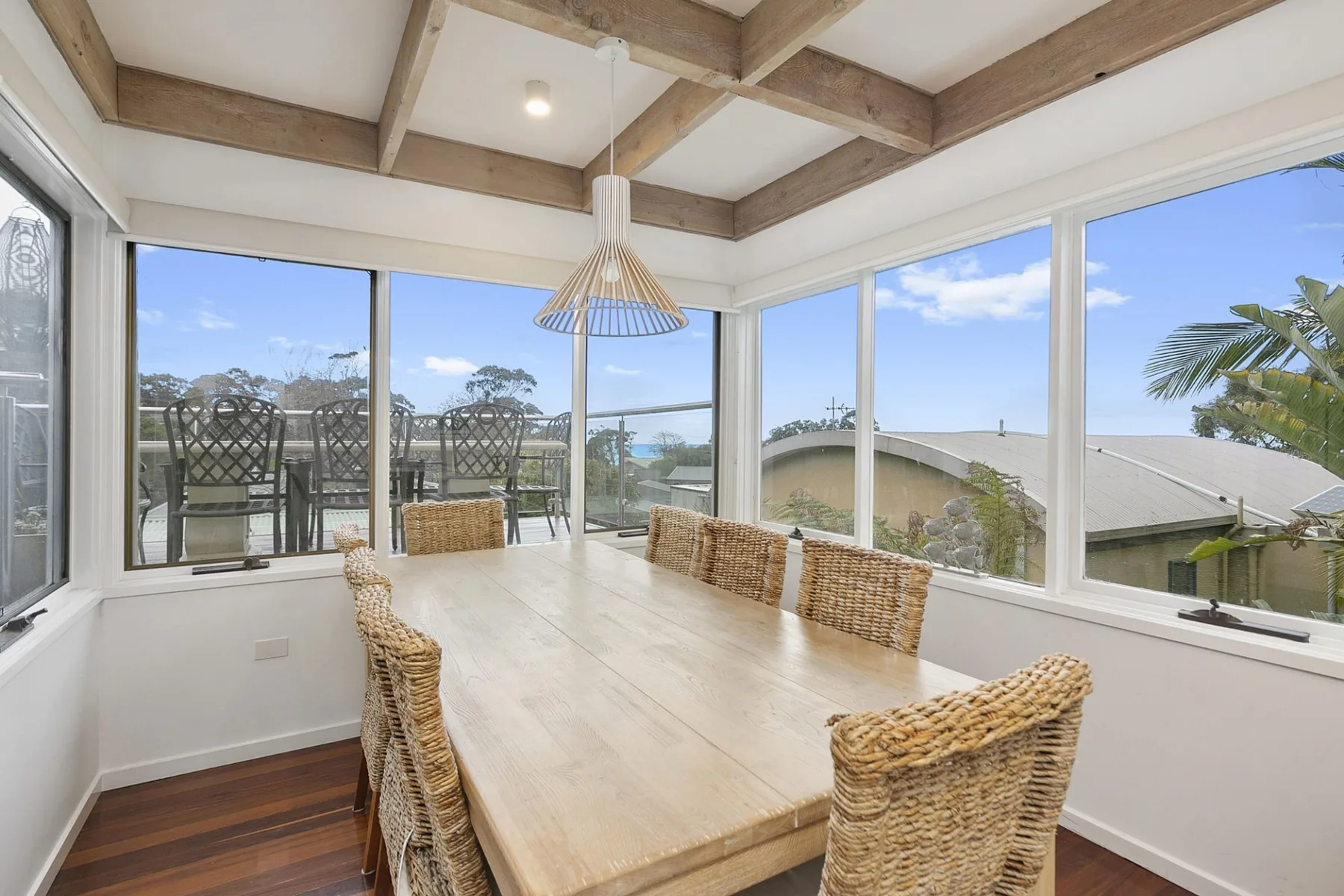 A sunlit dining area with a long table beside large windows.