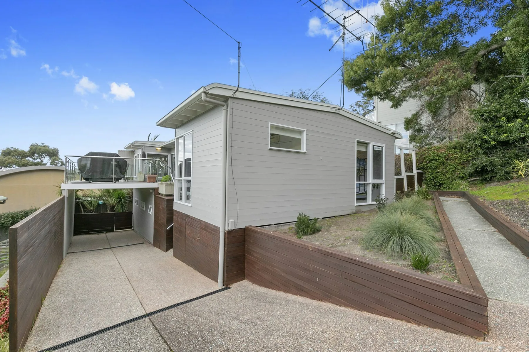 A small exterior building beside a paved walkway and raised garden beds.