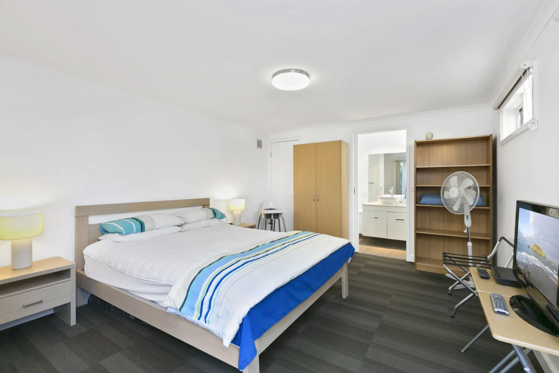 A bedroom with a bed, a desk, and a standing fan.