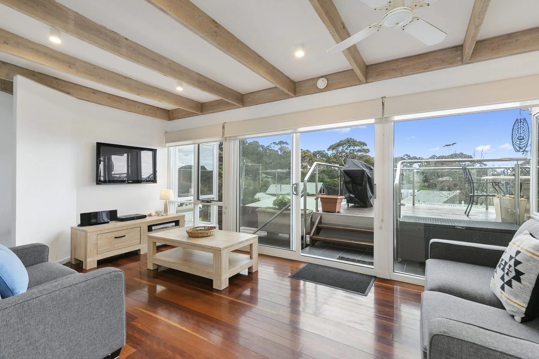 A bright living room opens onto a deck through wide glass doors.