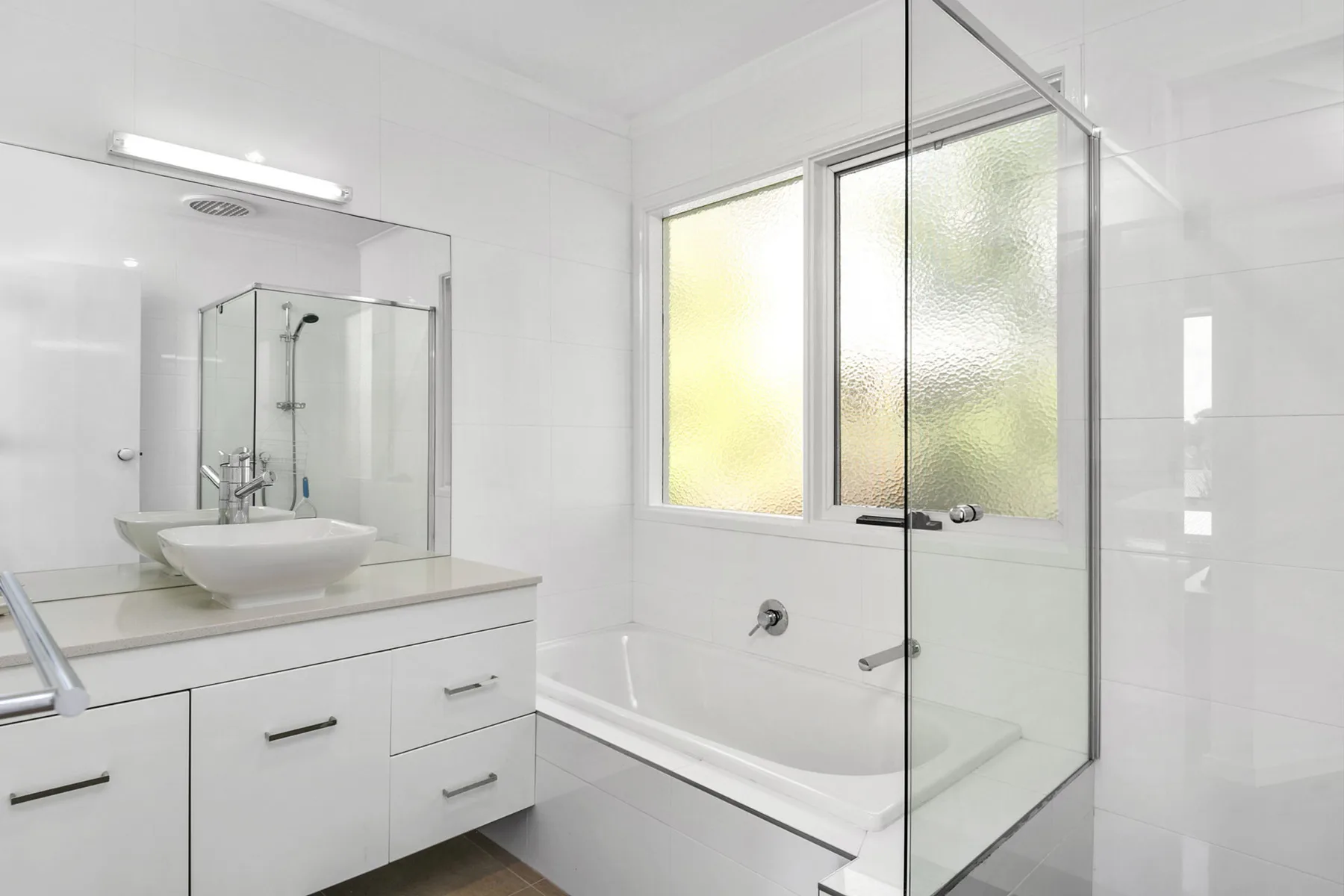 A bright bathroom with a bathtub and glass shower screen.