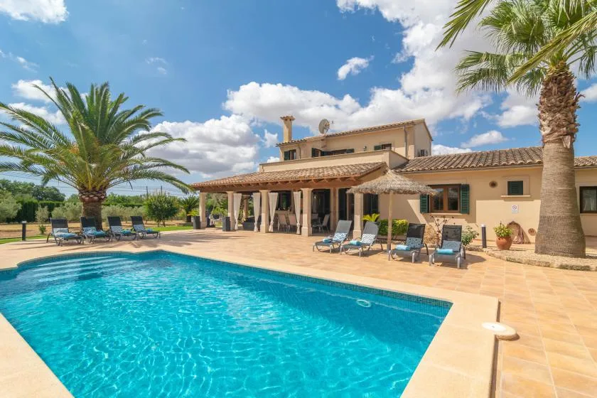 Una piscina junto a una casa, con asientos de descanso en el patio.