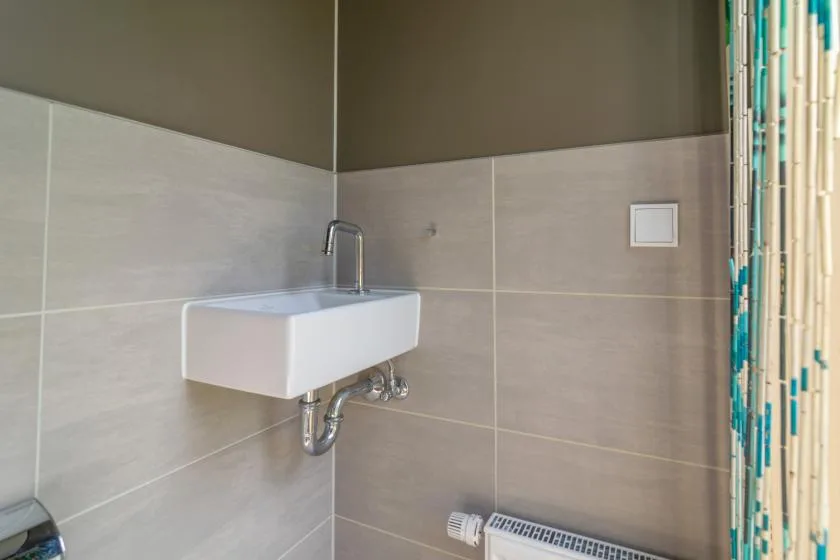 Esquina de un baño alicatado con lavabo de pared y cortina de ducha.