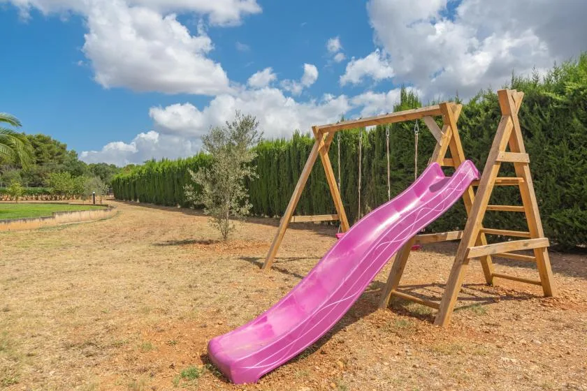 Una estructura de juego de madera con un tobogán rosa está en un patio seco.