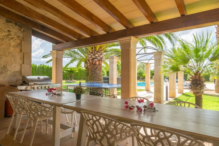 Una zona de comedor exterior cubierta da a un jardín y una piscina.