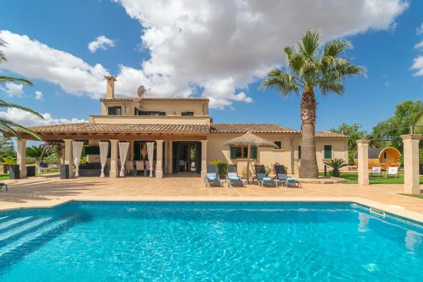 Una piscina frente a una casa, con asientos en el patio y una palmera.