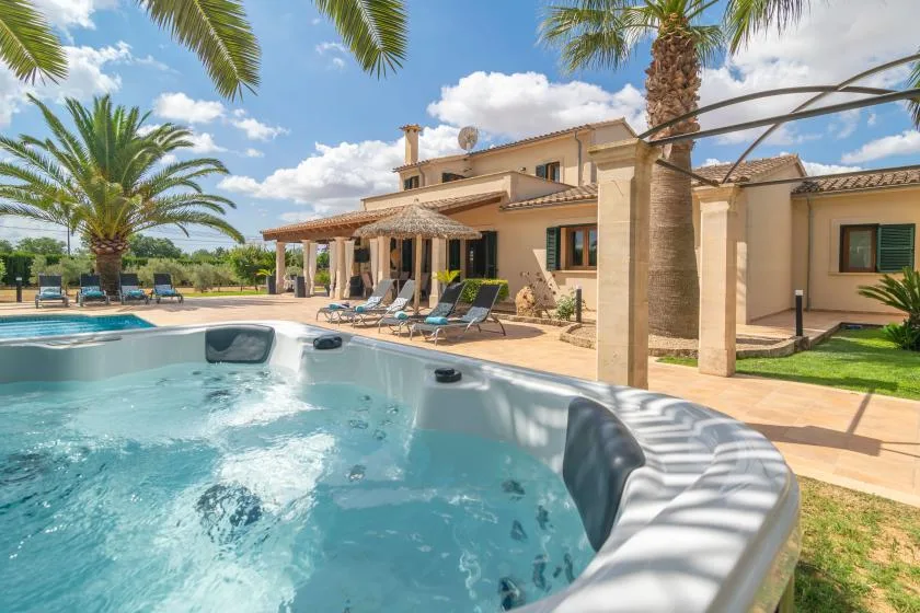 Una piscina y asientos al aire libre junto a una villa beige bajo palmeras.