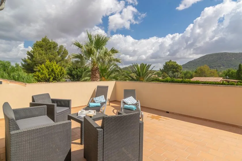 Una terraza al aire libre con asientos de mimbre y vistas a árboles y colinas.
