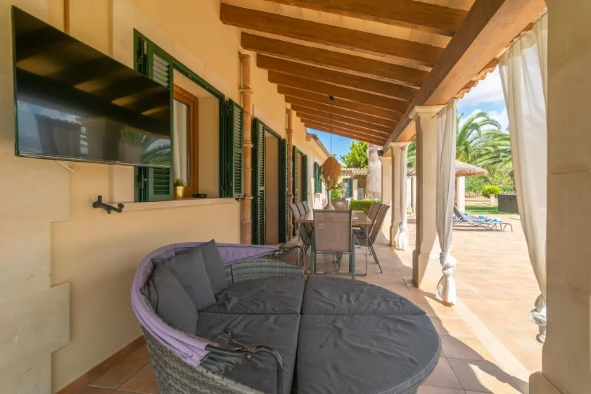 Un patio exterior cubierto con asientos acolchados y una mesa de comedor.