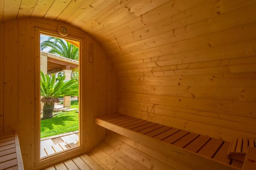 Una sauna de madera con un banco de listones y una puerta abierta al jardín.