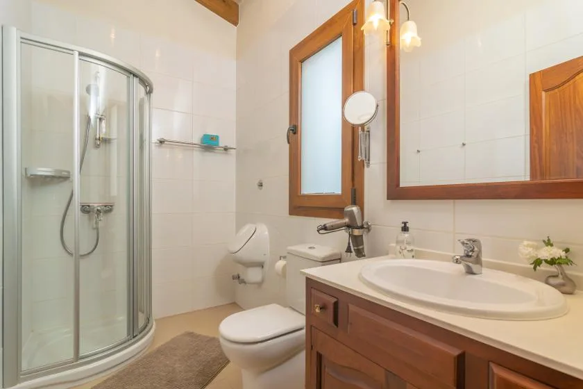 Un baño alicatado con una ducha de vidrio curvo y un mueble de madera.