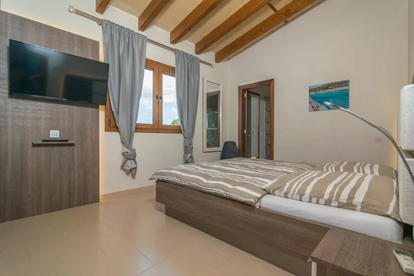 Un dormitorio con una cama doble, ropa de cama a rayas y un televisor en la pared.