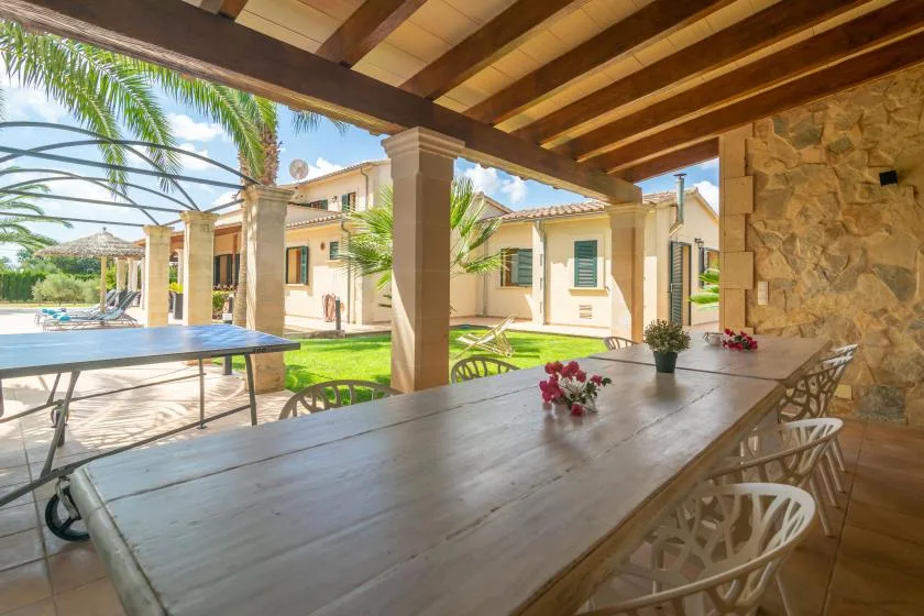Una zona de comedor exterior cubierta da a una piscina y un patio ajardinado.