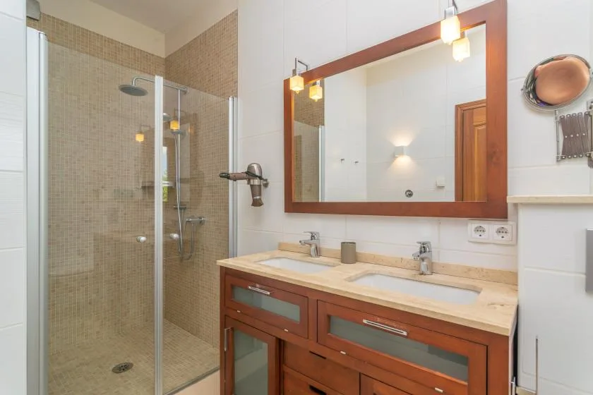 Un baño con ducha de vidrio, lavabo doble y un espejo grande.