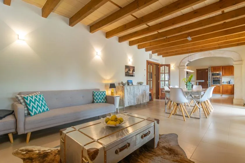 Una sala luminosa con un sofá gris y vigas de madera en el techo.