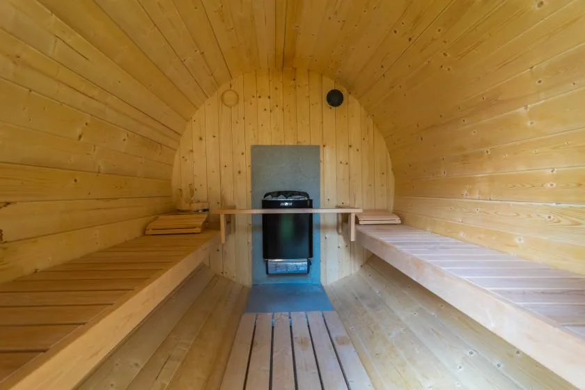Una sauna de madera con bancos junto a las paredes y un calentador al fondo.