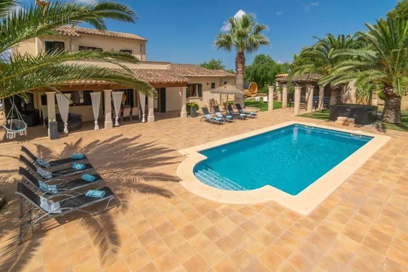 Una piscina al aire libre junto a un patio de baldosas, con asientos y palmeras.