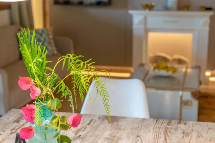Una sala de estar con asientos, una chimenea encendida y flores sobre la mesa.