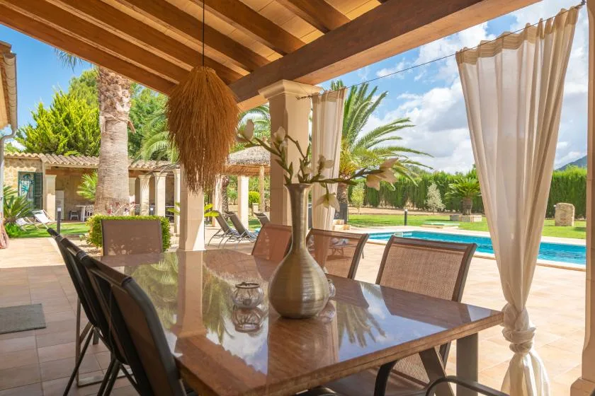 Una zona de comedor exterior cubierta da a una piscina y un jardín.
