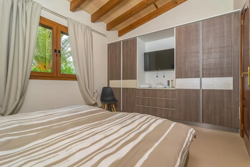 Un dormitorio con una colcha a rayas, una ventana con cortinas y armarios empotrados.