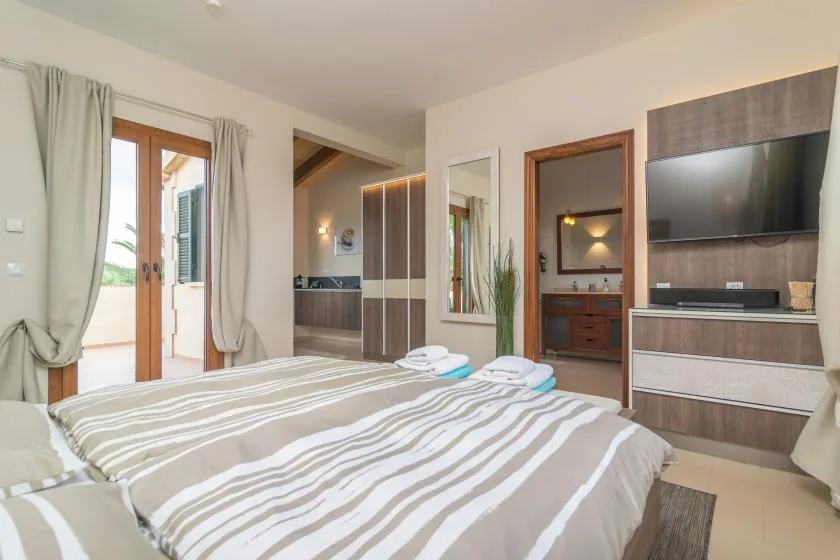 Un dormitorio con ropa de cama a rayas, un televisor y una puerta a una habitación contigua.
